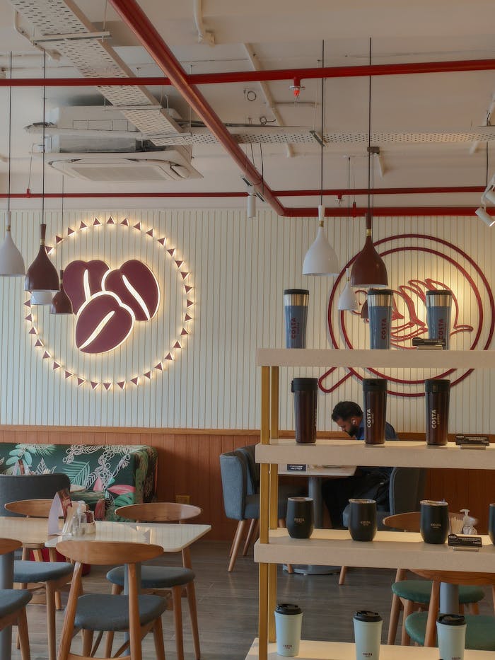 hero-img-01 Stylish café interior featuring modern furniture and coffee-themed decor, ideal for cozy gatherings.